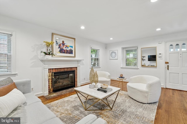 living area with wood finished floors, a brick fireplace, and recessed lighting