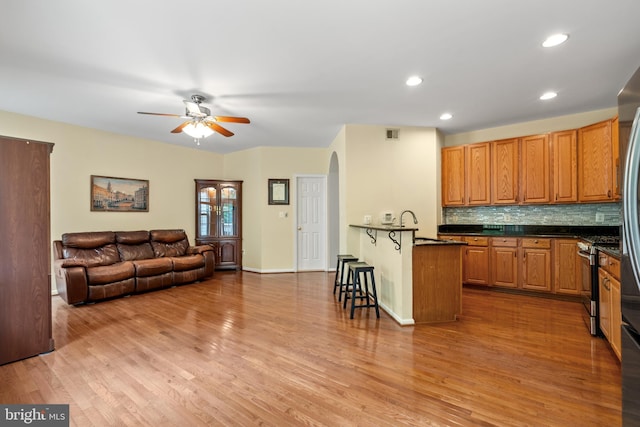 kitchen with a ceiling fan, open floor plan, a kitchen bar, arched walkways, and light wood-style flooring