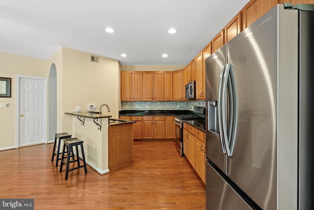 kitchen with appliances with stainless steel finishes, a sink, a breakfast bar area, light wood-style floors, and recessed lighting