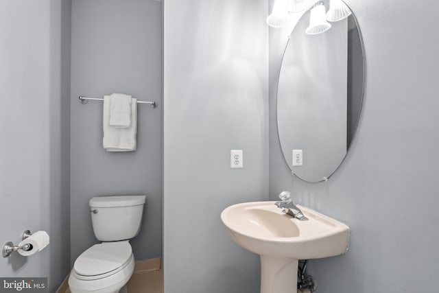 half bathroom featuring toilet, tile patterned flooring, baseboards, and a sink