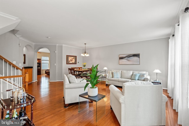 living room featuring arched walkways, wood finished floors, stairs, a chandelier, and crown molding