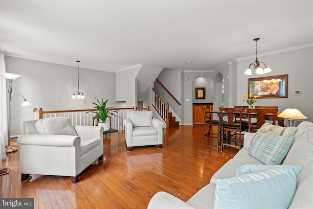 living room featuring a chandelier, hardwood / wood-style floors, arched walkways, crown molding, and stairs