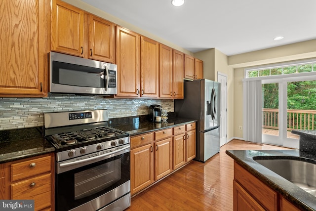 kitchen featuring appliances with stainless steel finishes, light wood-style flooring, decorative backsplash, dark stone counters, and recessed lighting