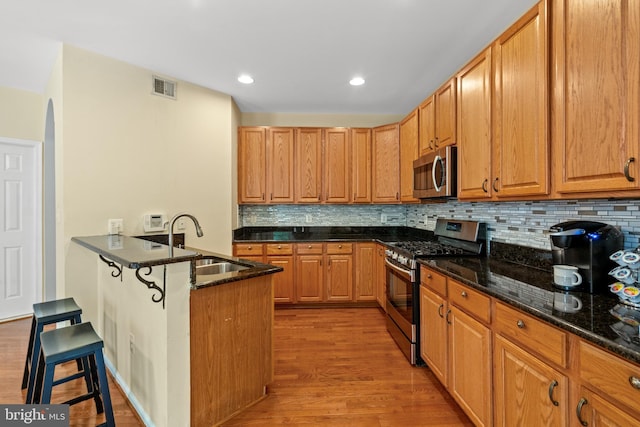 kitchen with stainless steel appliances, a sink, light wood-style flooring, a breakfast bar area, and dark stone counters