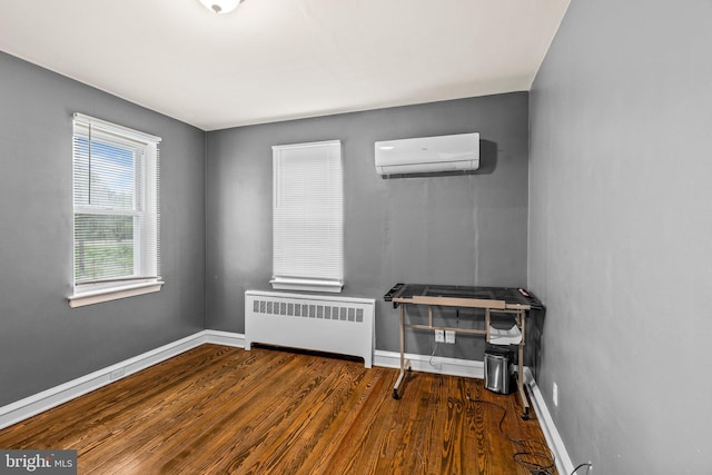 empty room with radiator heating unit, a wall unit AC, wood finished floors, and baseboards