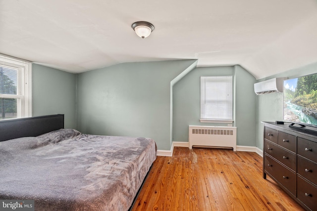 bedroom featuring radiator, light wood-style flooring, lofted ceiling, an AC wall unit, and baseboards