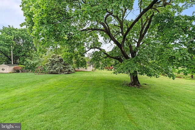 view of green lawn with a playground, an outbuilding, and a storage unit
