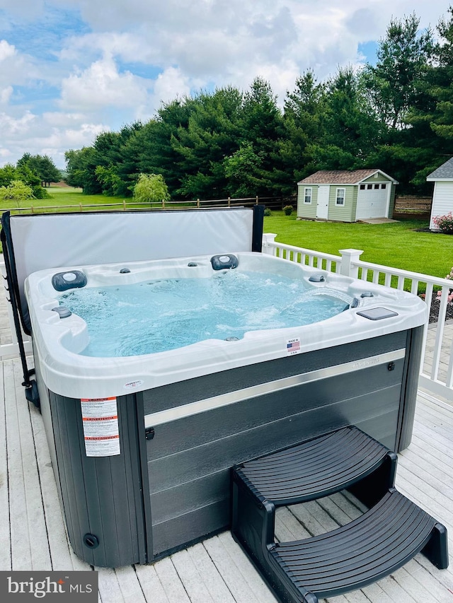 wooden terrace featuring a hot tub, a lawn, and an outbuilding