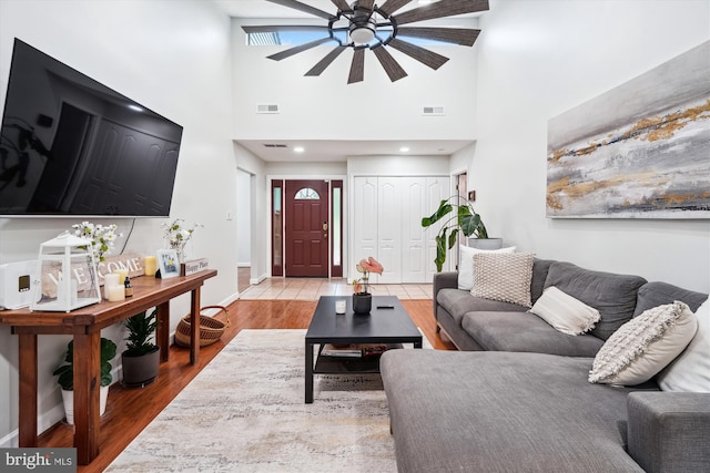 living room with a ceiling fan, a high ceiling, light wood finished floors, and baseboards