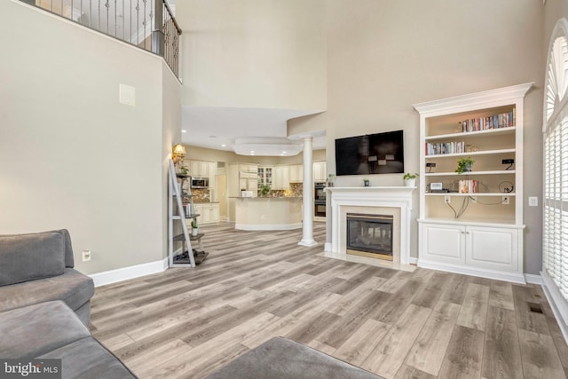 12723 Lady Somerset Ln, Fairfax, VA 22033 - living area featuring a high ceiling, light wood-style flooring, a glass covered fireplace, baseboards, and ornate columns