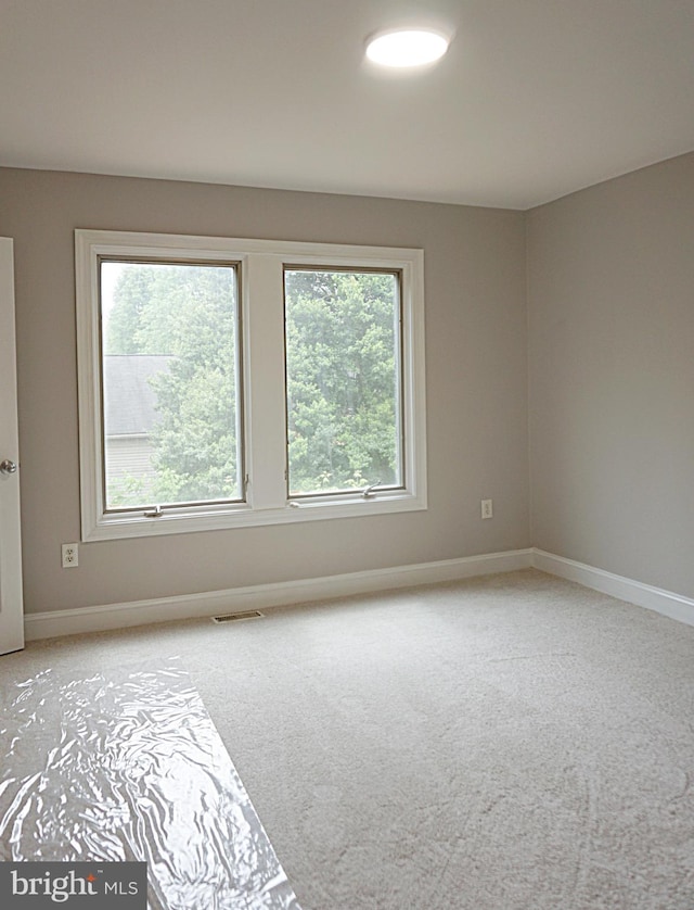 spare room featuring light carpet and baseboards