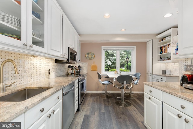 kitchen with appliances with stainless steel finishes, a sink, baseboards, white cabinets, and backsplash
