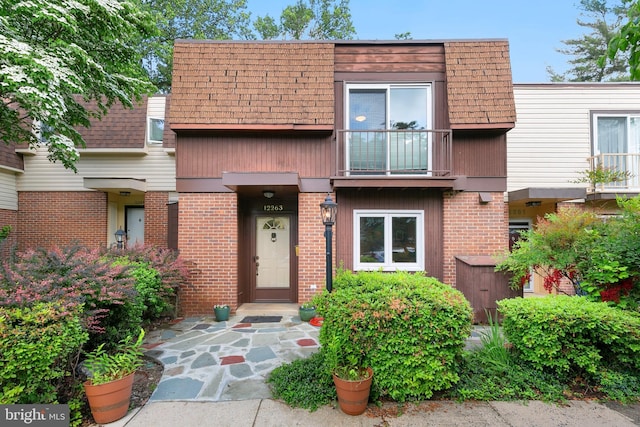 view of front of home featuring mansard roof, roof with shingles, and brick siding