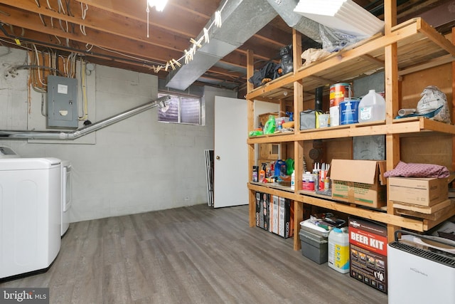 unfinished basement with electric panel, wood finished floors, washing machine and dryer, and concrete block wall