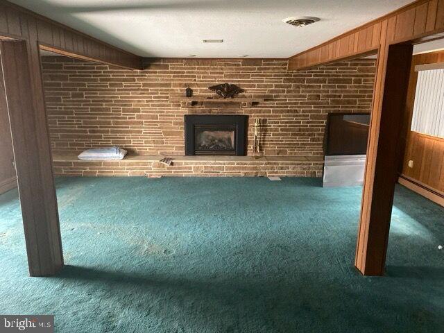 12003 Warner Rd, Ladiesburg, MD 21759 - unfurnished living room featuring carpet, wood walls, a brick fireplace, and brick wall