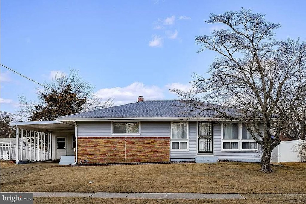 ranch-style home featuring roof with shingles, a front yard, brick siding, and a chimney