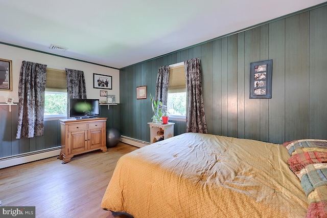 bedroom with a baseboard radiator, light wood-style floors, and wood walls