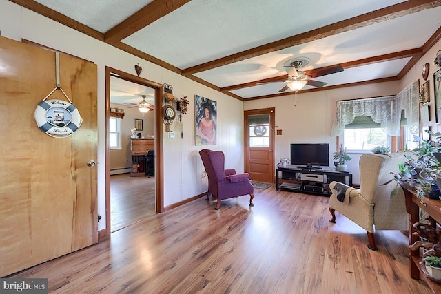 living area featuring a ceiling fan, healthy amount of natural light, light wood-style floors, and beamed ceiling
