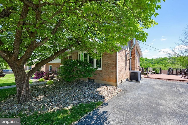 view of property exterior featuring brick siding, central AC unit, a deck, and asphalt driveway