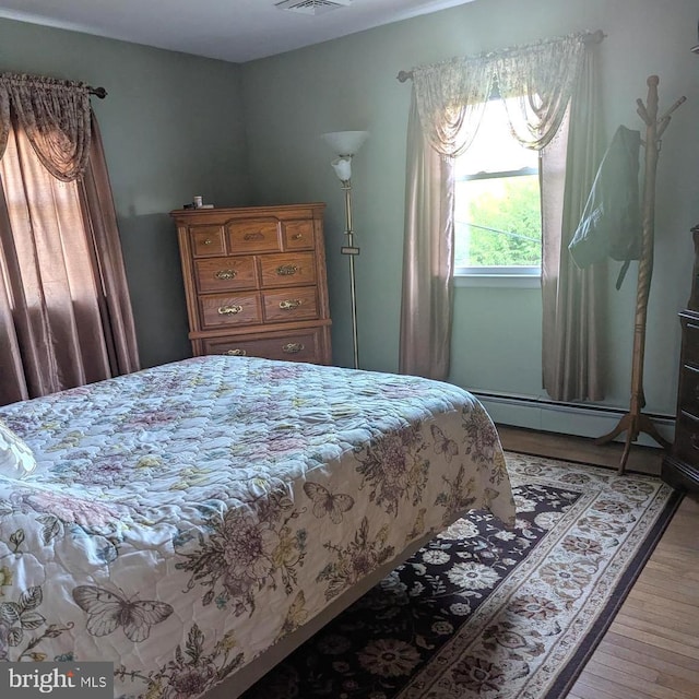 bedroom with a baseboard heating unit and light wood-style flooring