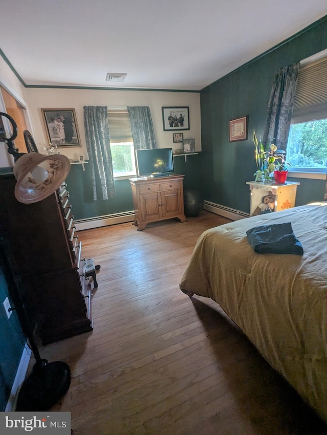 bedroom with a baseboard heating unit, multiple windows, and light wood-type flooring