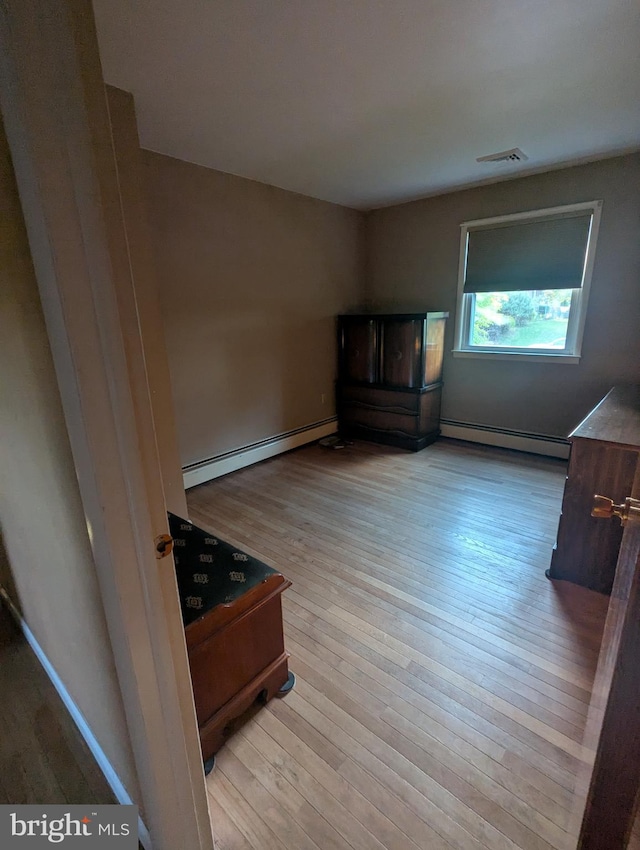 unfurnished bedroom with a baseboard heating unit and hardwood / wood-style floors