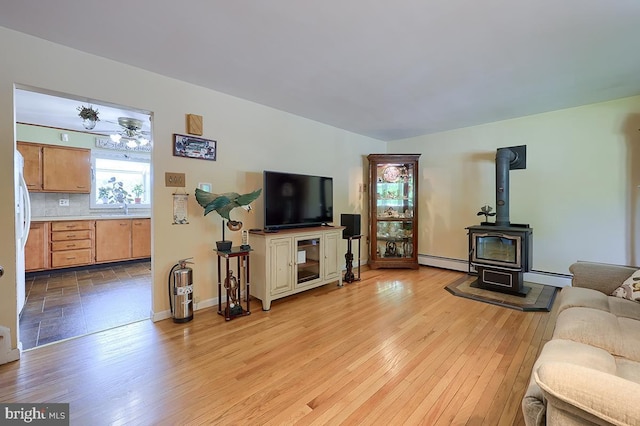 living area featuring a baseboard radiator, light wood finished floors, and a wood stove