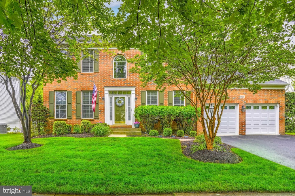 view of front of house with driveway, a garage, a front yard, brick siding, and central air condition unit
