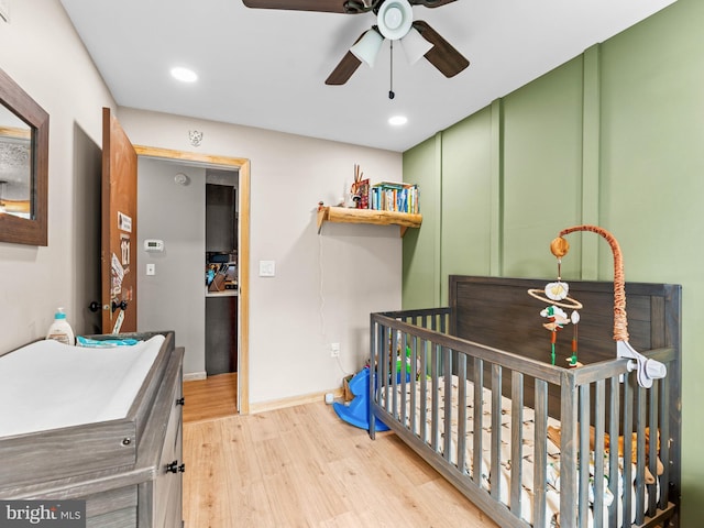 bedroom with wood finished floors, a crib, baseboards, recessed lighting, and a ceiling fan