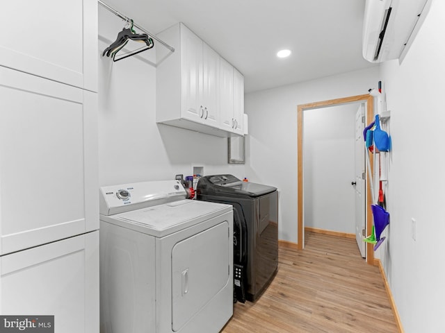 clothes washing area with washer and clothes dryer, cabinet space, light wood-style flooring, an AC wall unit, and baseboards