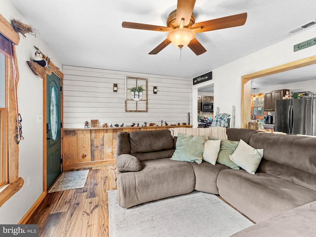 living room with a ceiling fan, wood finished floors, wood walls, and baseboards