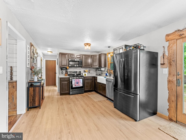 kitchen with appliances with stainless steel finishes, light countertops, a sink, light wood finished floors, and a textured ceiling