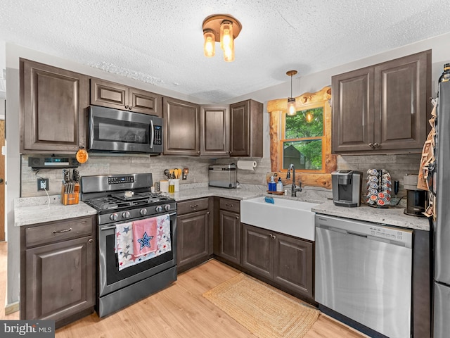 kitchen with appliances with stainless steel finishes, a textured ceiling, light wood finished floors, backsplash, and a sink