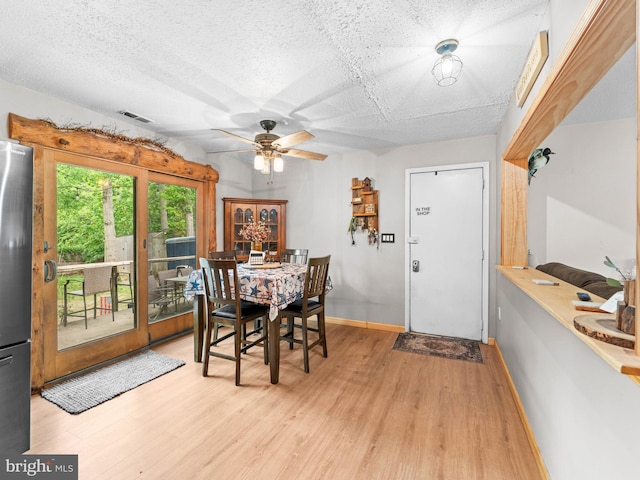 dining room featuring ceiling fan, light wood-style flooring, a textured ceiling, and baseboards