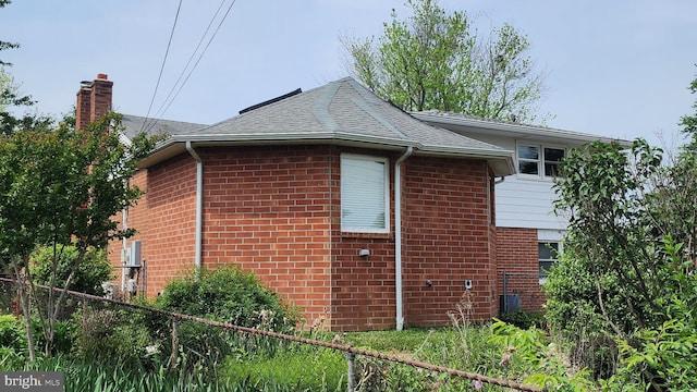 view of home's exterior with brick siding, fence, a chimney, and roof with shingles