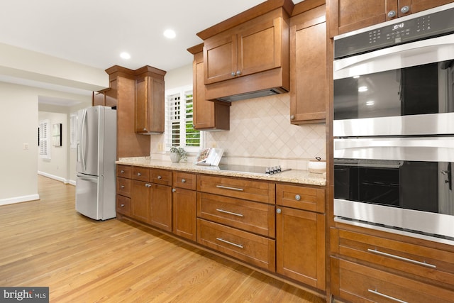 1802 24th St S, Arlington, VA 22202 - kitchen with appliances with stainless steel finishes, light wood finished floors, brown cabinets, decorative backsplash, and light stone counters