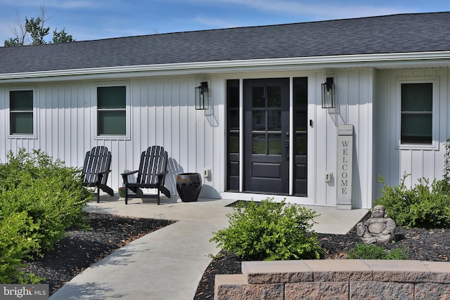 view of exterior entry with board and batten siding and roof with shingles