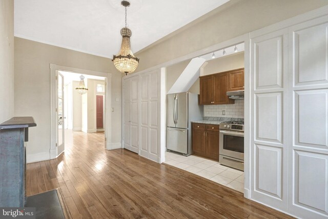 812 E St SE, Washington, DC 20003 - kitchen featuring appliances with stainless steel finishes, a chandelier, under cabinet range hood, decorative backsplash, and light wood finished floors