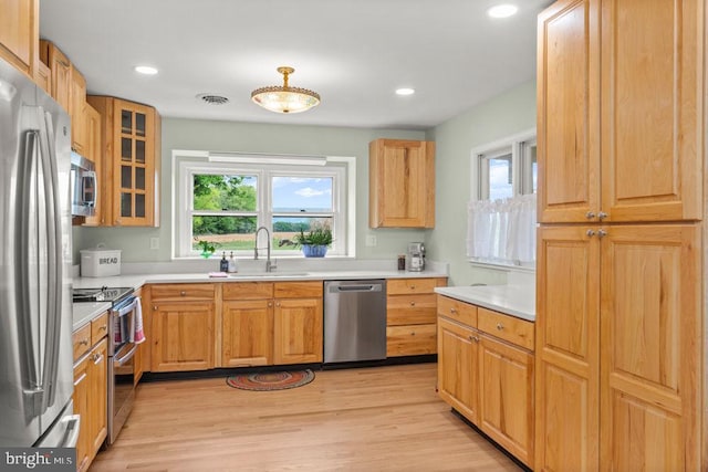 kitchen with stainless steel appliances, a sink, light wood finished floors, light countertops, and glass insert cabinets
