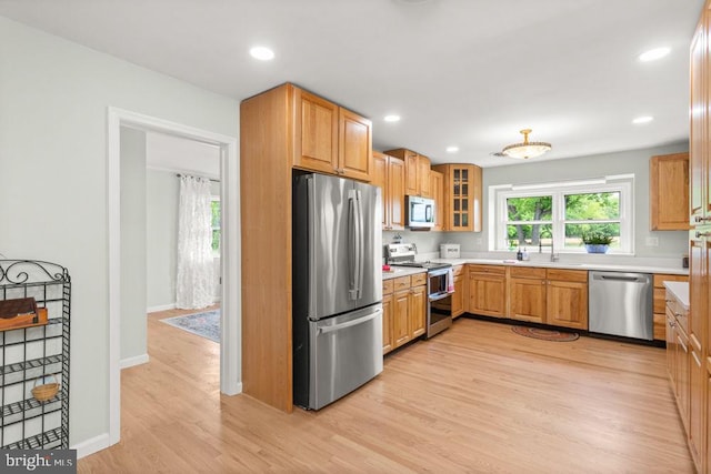 kitchen with appliances with stainless steel finishes, light wood-style floors, light countertops, glass insert cabinets, and recessed lighting