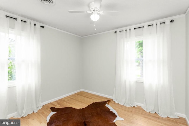 spare room with light wood finished floors, baseboards, ornamental molding, and ceiling fan