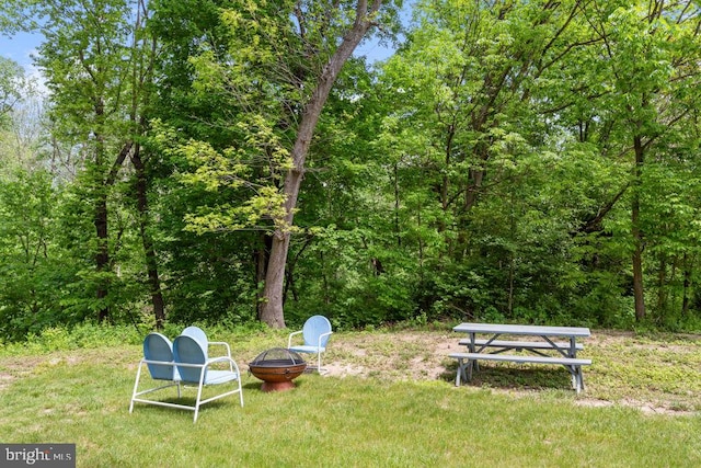 view of yard featuring an outdoor fire pit and a wooded view