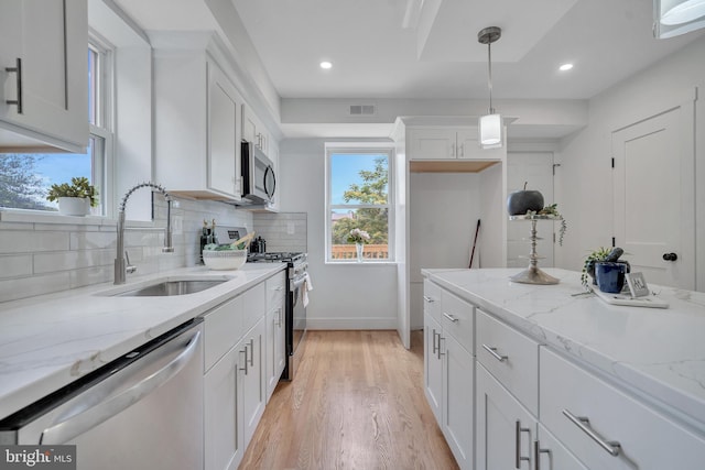 1636 40th St SE, Washington, DC 20020 - kitchen featuring stainless steel appliances, a sink, backsplash, light wood finished floors, and white cabinetry