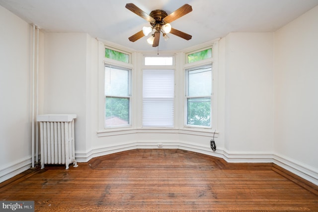 empty room featuring radiator heating unit, a ceiling fan, and wood finished floors