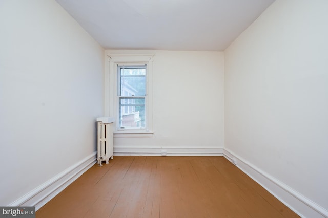 empty room featuring radiator heating unit, hardwood / wood-style floors, and baseboards