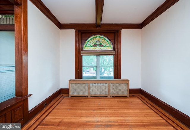 unfurnished room with light wood-type flooring, beam ceiling, crown molding, and baseboards
