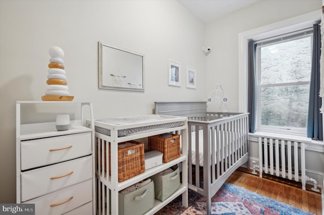 bedroom with radiator, a crib, multiple windows, and wood finished floors