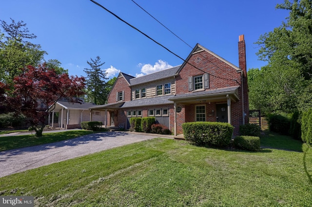 view of front of home with a chimney, brick siding, a front yard, and asphalt driveway