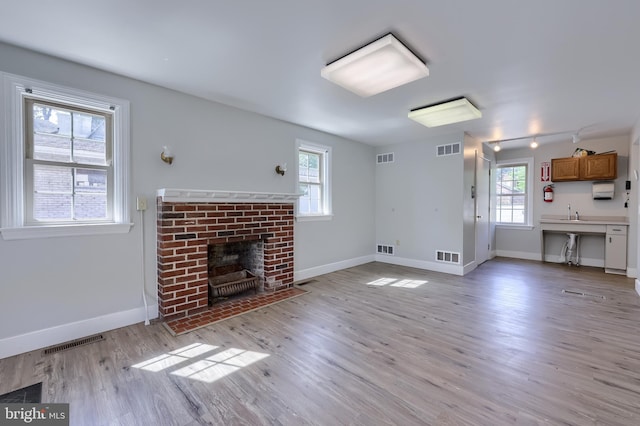 unfurnished living room featuring plenty of natural light, a brick fireplace, light wood-style flooring, and baseboards
