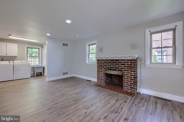 unfurnished living room with independent washer and dryer, baseboards, light wood-style flooring, a brick fireplace, and recessed lighting